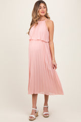 woman wearing a blush pink pleated maternity dress with a flowing halter neckline and visible baby bump