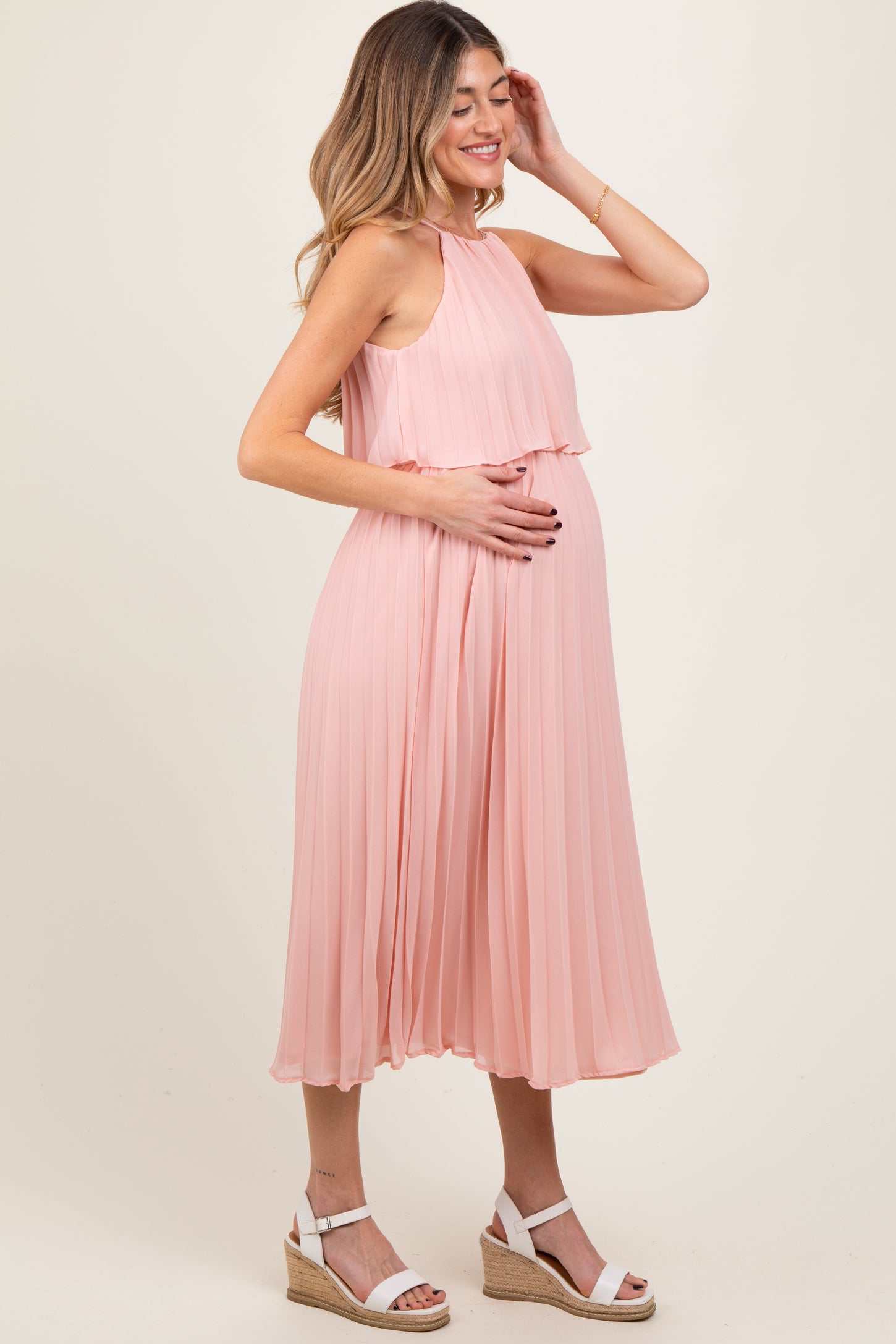 woman wearing a light pink pleated maternity dress and holding her baby bump