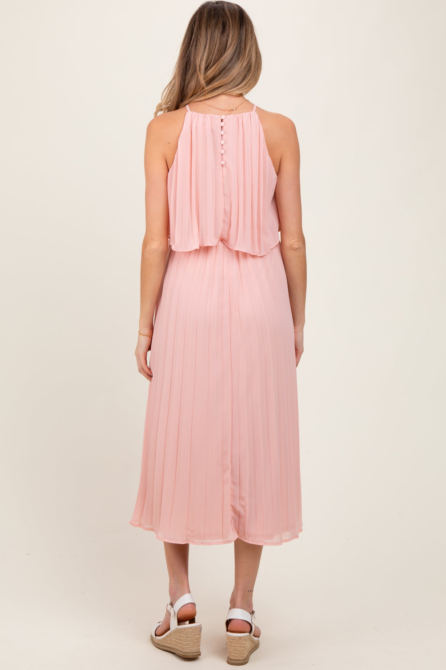 woman wearing a pink pleated maternity dress with a back button detail and a flowing silhouette