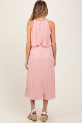 woman wearing a pink pleated maternity dress with a back button detail and a flowing silhouette
