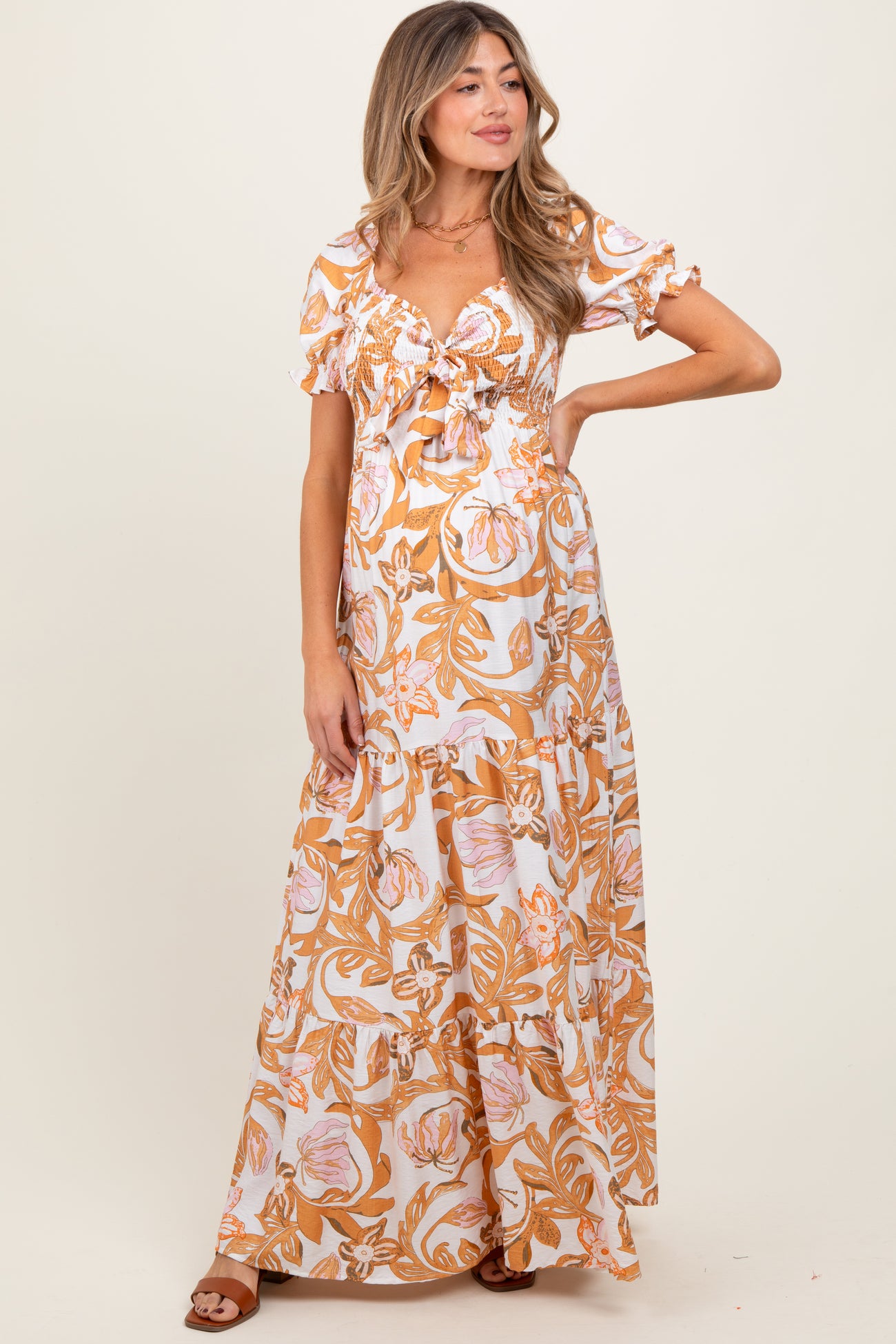 woman wearing a floral print orange and white maxi maternity dress with short ruffled sleeves and a smocked bodice