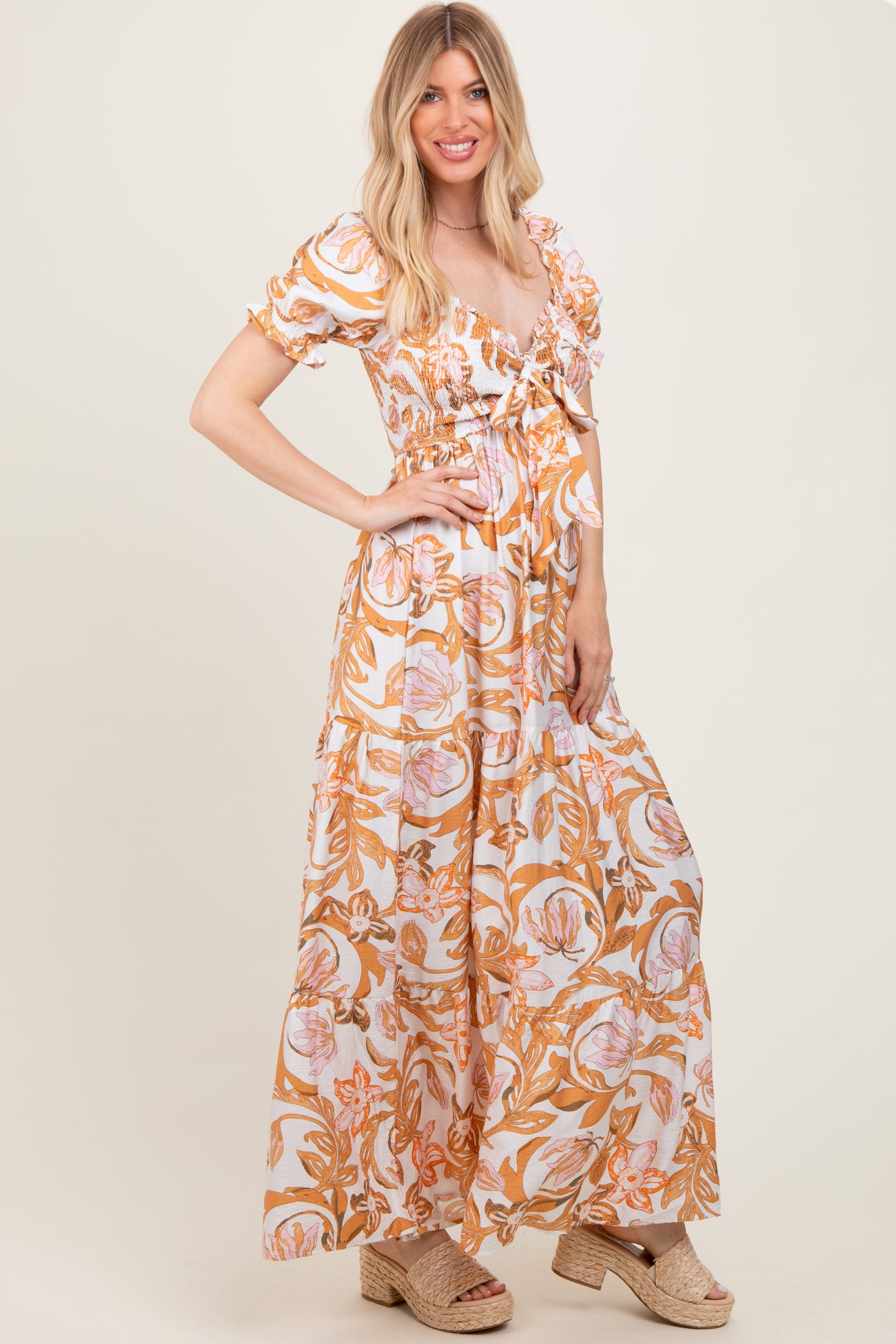 woman wearing a white maxi dress with orange floral print and puff sleeves, styled with beige espadrille wedges