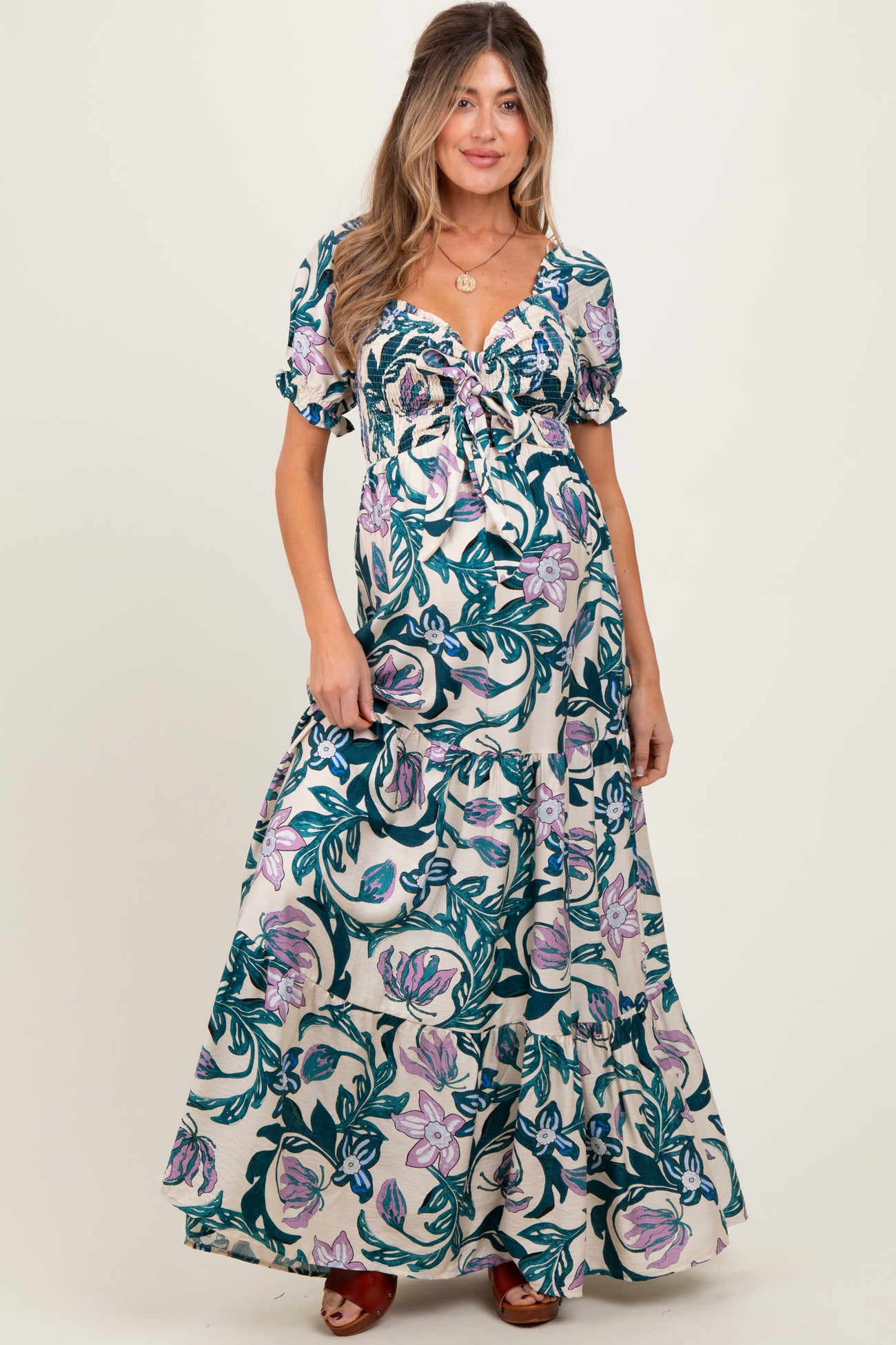 woman wearing a floral print maternity maxi dress with a tie detail and puff sleeves, showcasing her baby bump