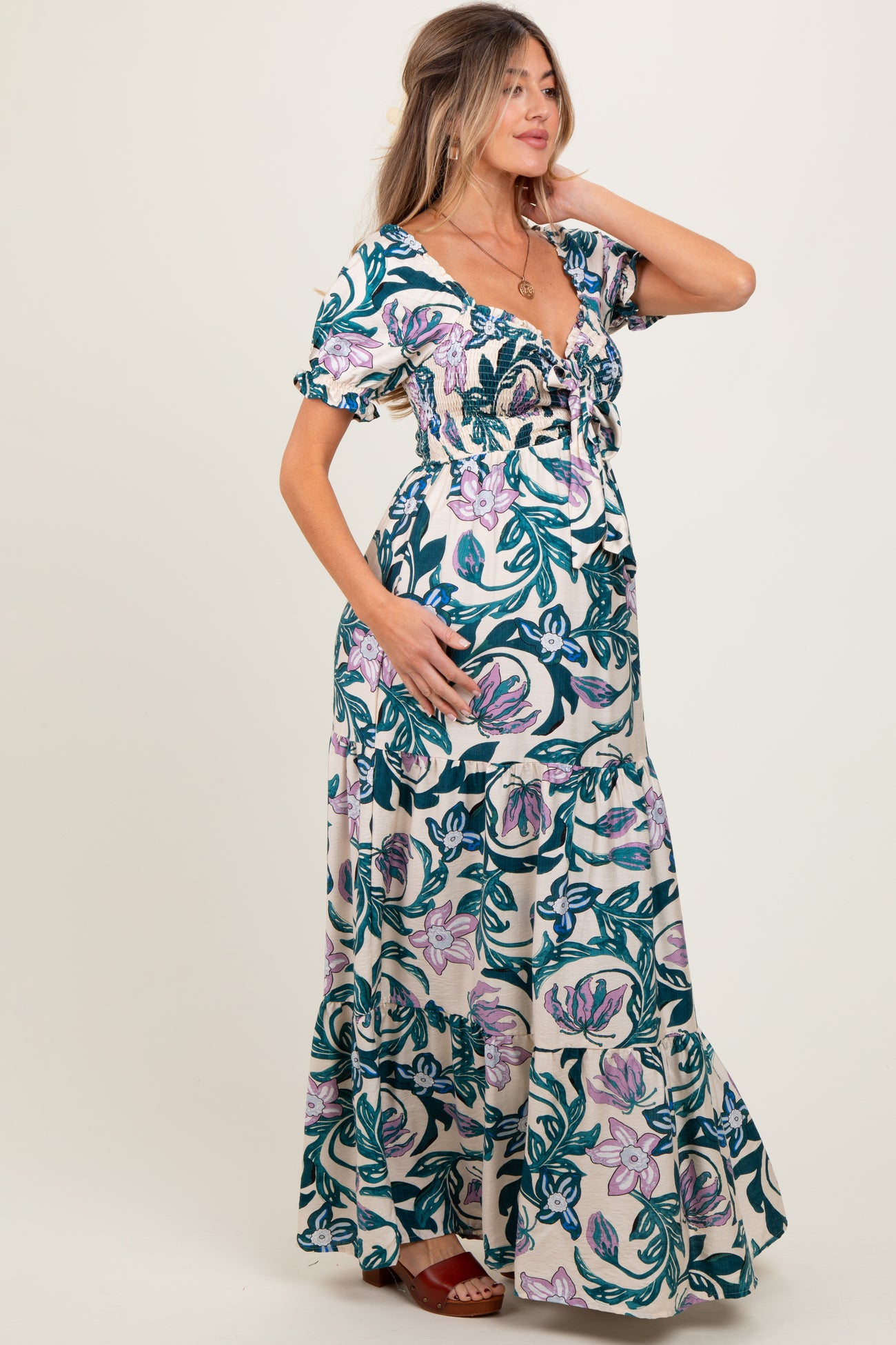 woman wearing a floral maternity maxi dress with a fitted bodice and ruffled sleeves, cradling her baby bump