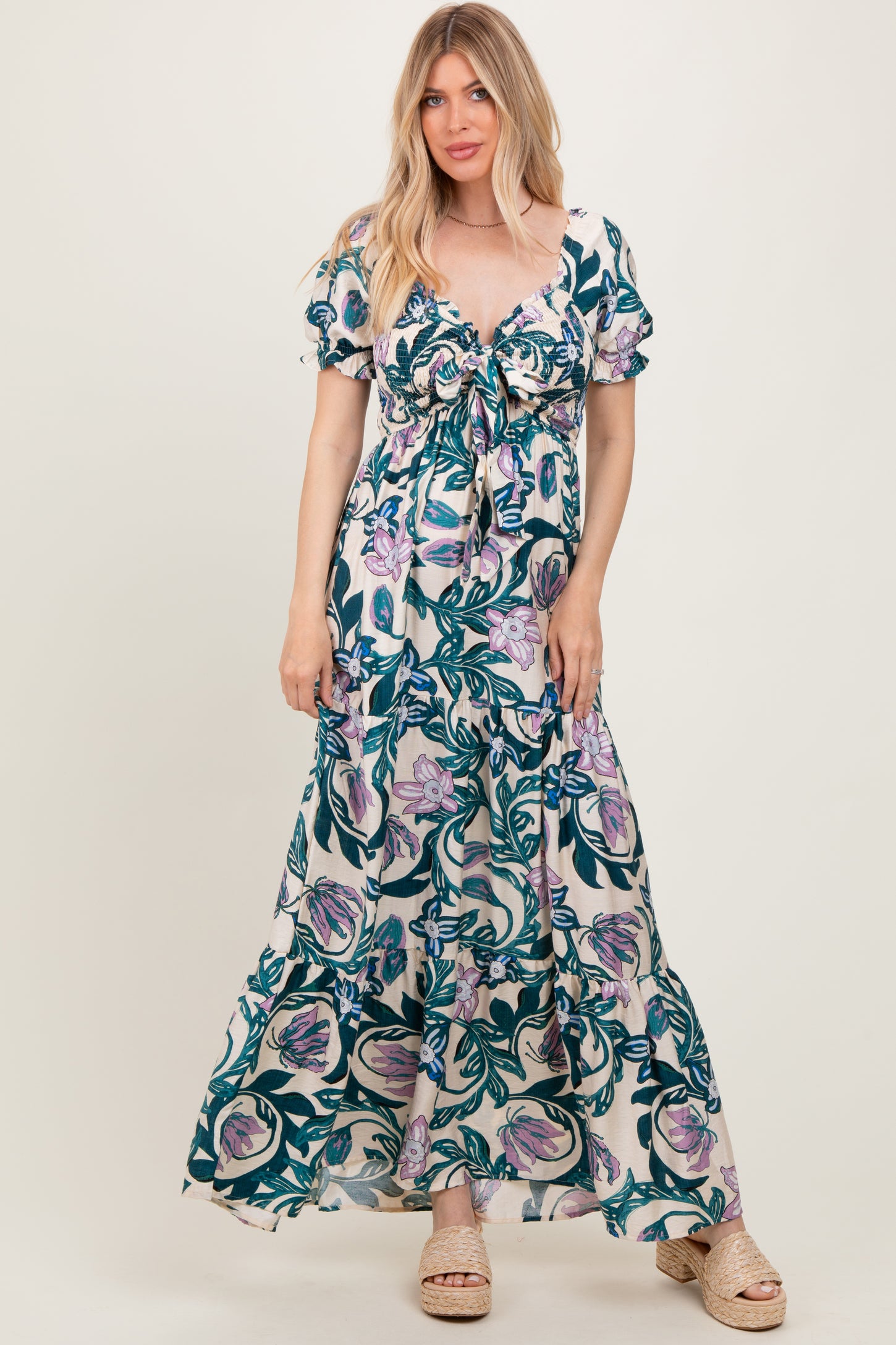 woman wearing a floral maxi dress with puff sleeves and a tie front detail, standing on a light background
