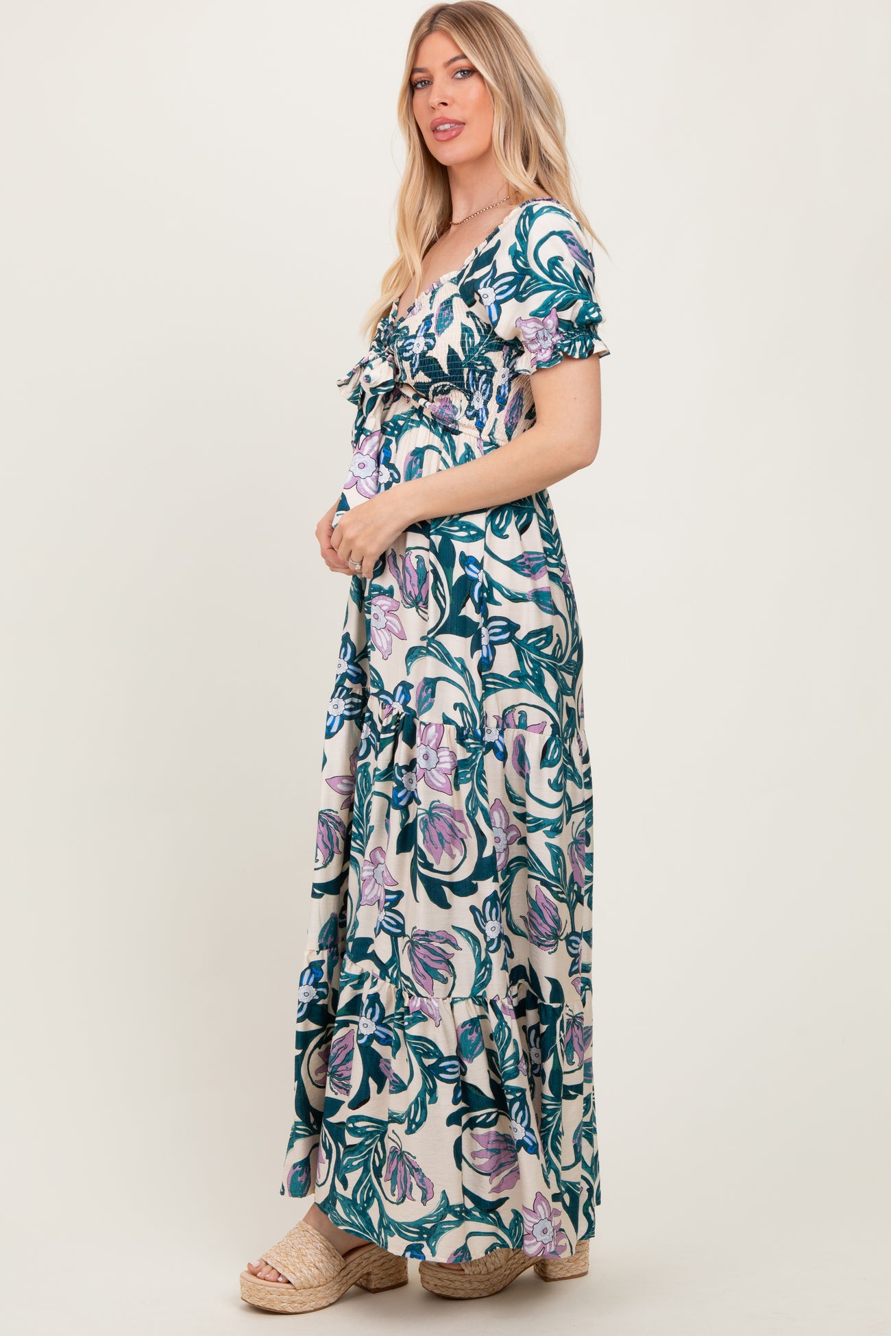 woman wearing a floral maxi dress with short sleeves and ruffle details, standing sideways and smiling