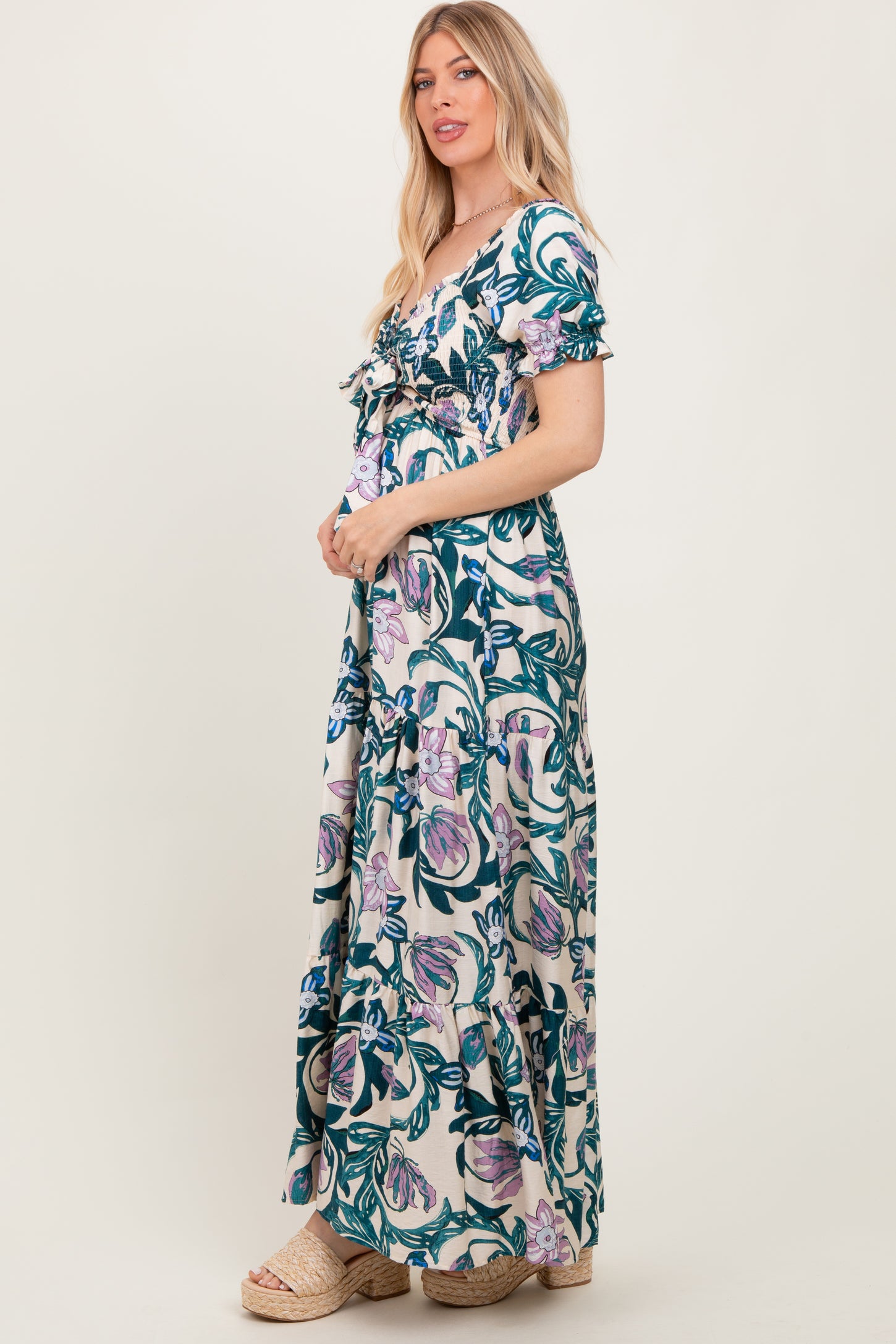 woman wearing a floral maxi dress with short sleeves and ruffle details, standing sideways and smiling