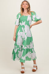 woman wearing a green floral midi dress with puff sleeves and smocked bodice, standing and smiling