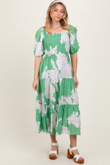 woman wearing a green floral mid-length dress with puff sleeves and a smocked bodice, standing against a neutral background