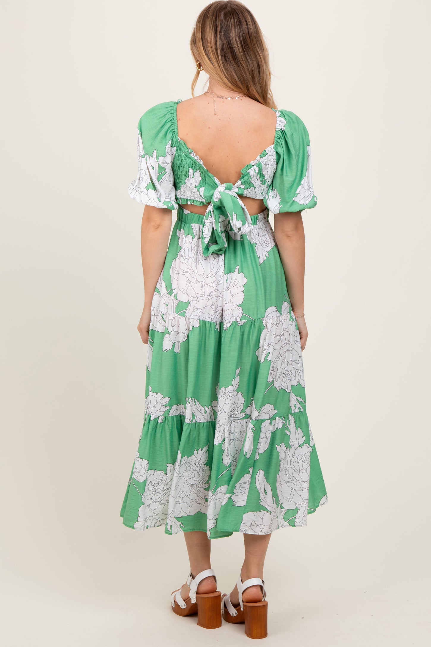 woman wearing a green floral maxi dress with puff sleeves and an open back, viewed from behind