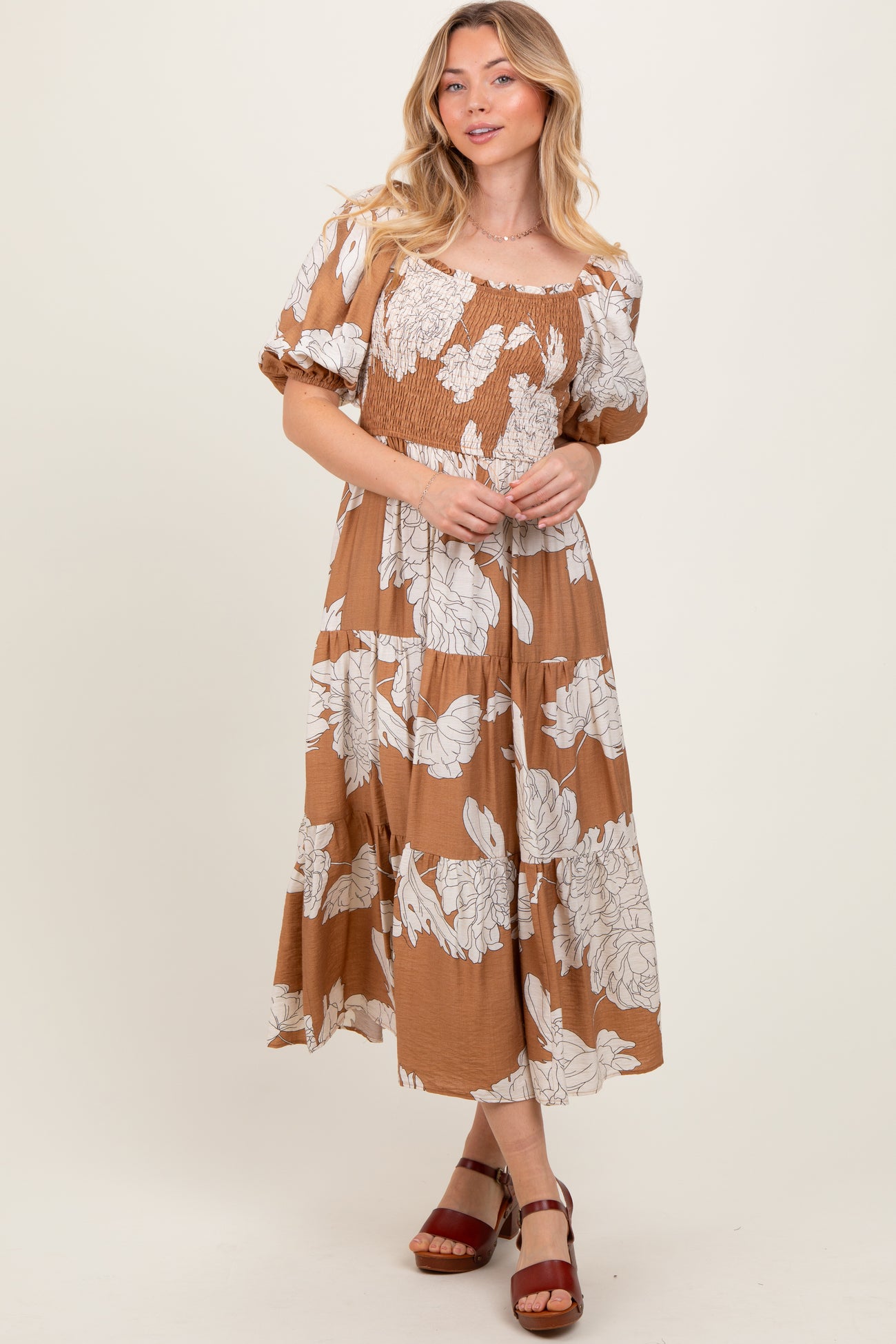 woman wearing a brown floral maxi dress with a smocked bodice and puff sleeves, standing in a relaxed pose