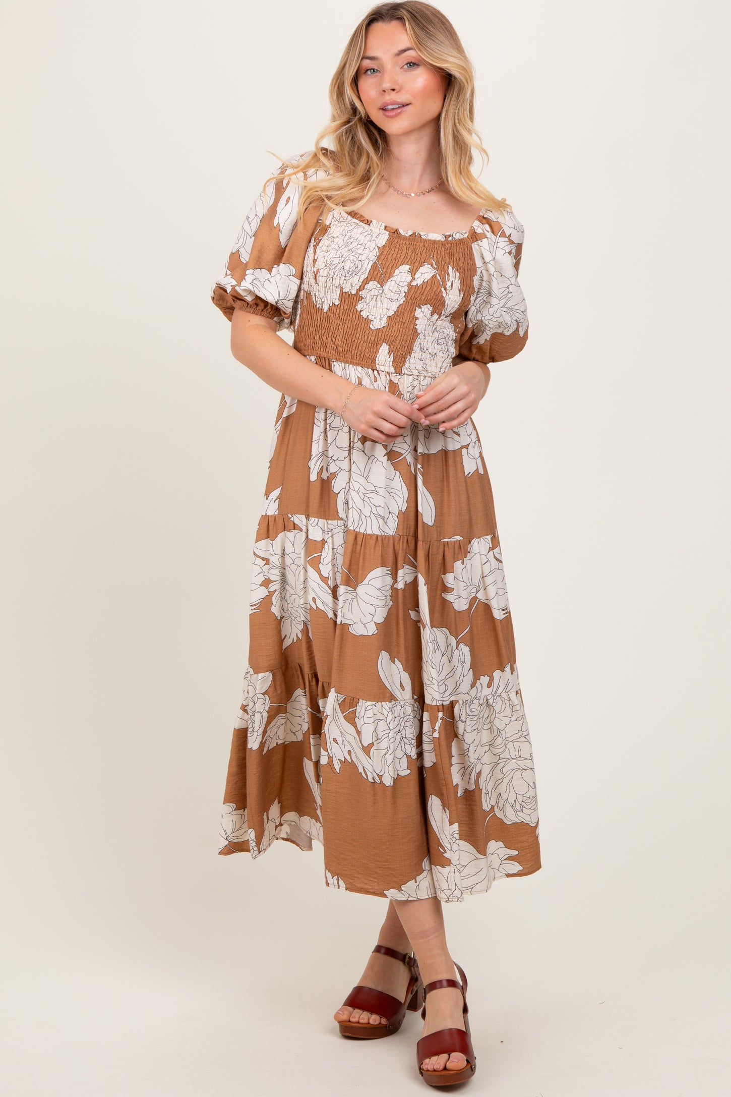 woman wearing a brown floral maxi dress with a smocked bodice and puff sleeves, standing in a relaxed pose