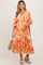 woman wearing an orange and white floral print maternity dress with puff sleeves and a tiered skirt, holding a straw bag