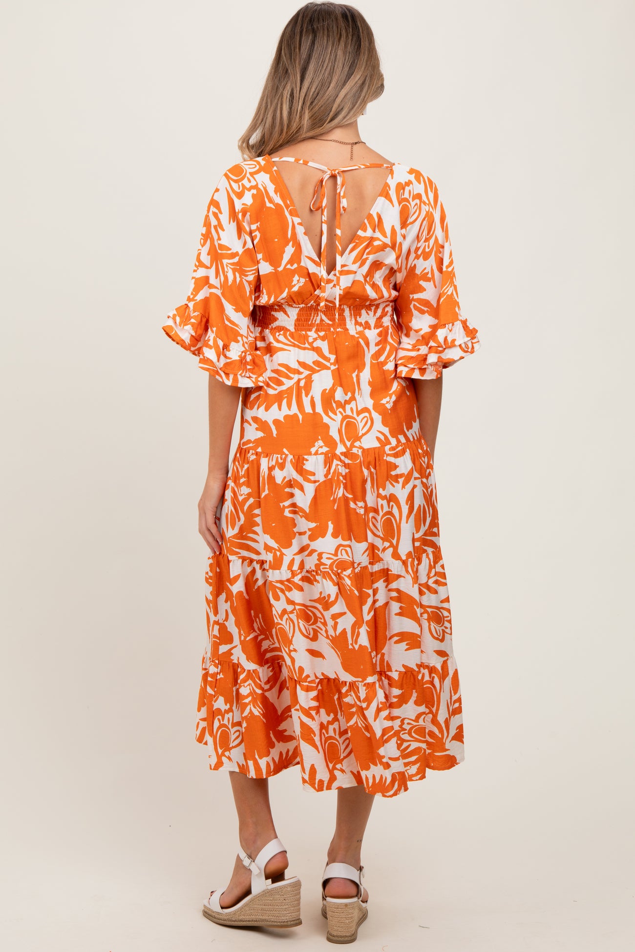 woman wearing an orange and white floral maternity dress with ruffled sleeves and a tie detail at the back