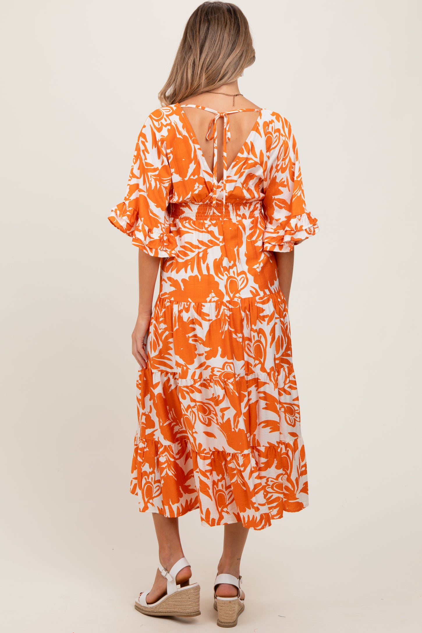 woman wearing an orange and white floral maternity dress with ruffled sleeves and a tie detail at the back