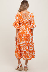 woman wearing an orange and white floral maternity dress with ruffled sleeves and a tie detail at the back