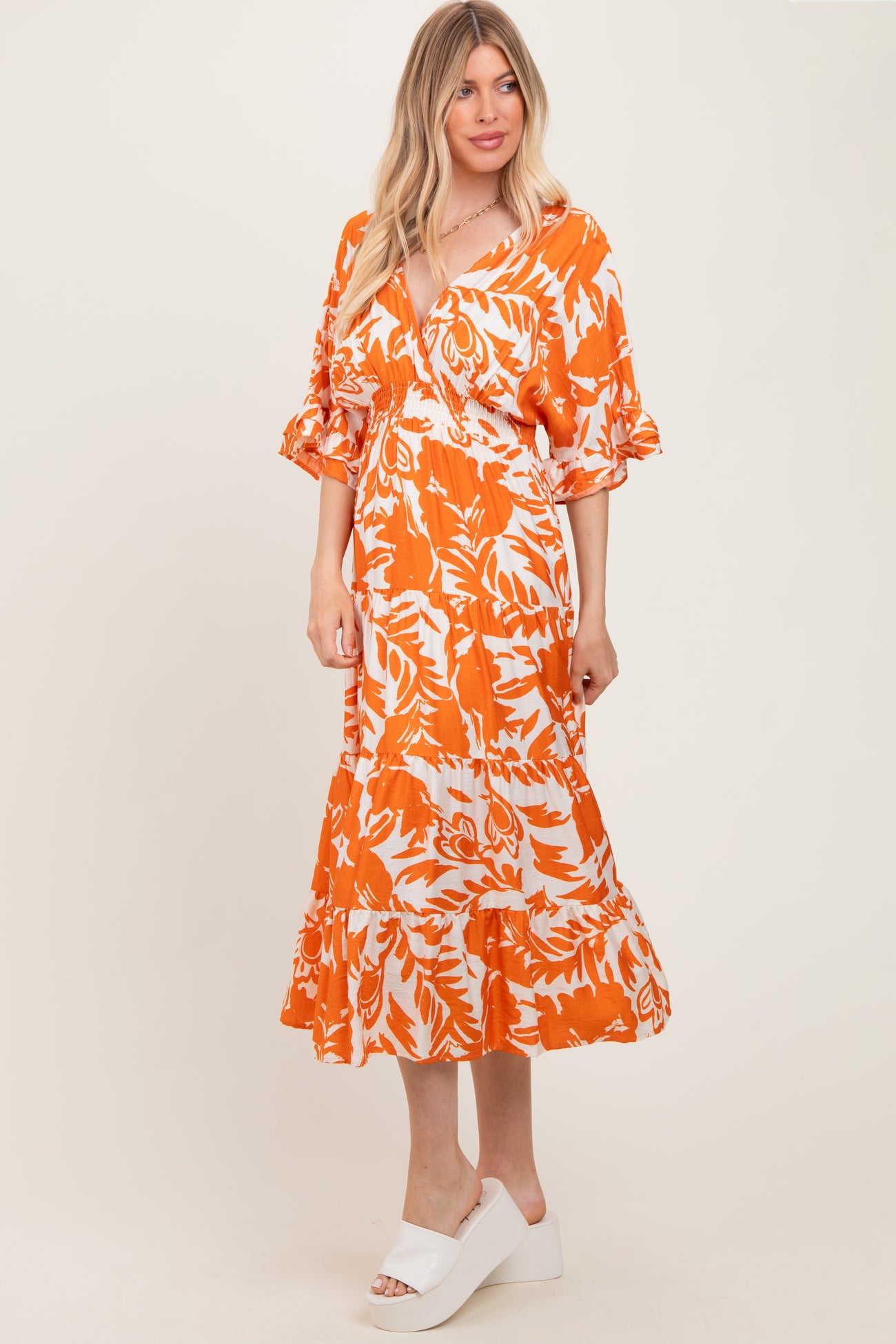 woman wearing an orange and white floral print maxi dress with ruffled sleeves and a flowing skirt