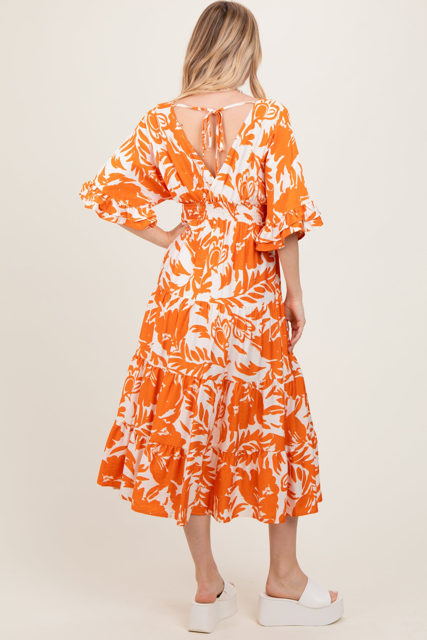 woman wearing an orange floral print maxi dress with puff sleeves and a tie-back detail