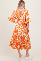 woman wearing an orange floral print maxi dress with puff sleeves and a tie-back detail