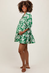 woman wearing a green floral maternity dress with short sleeves and a tiered skirt, showing her baby bump