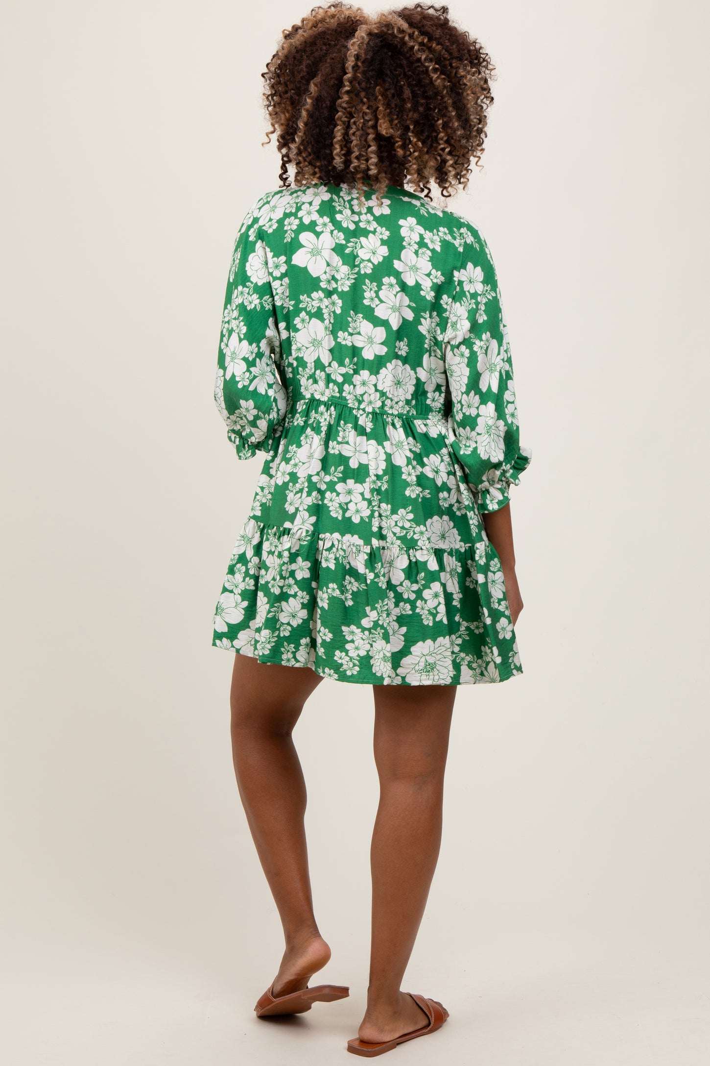 woman wearing a green floral maternity dress with a tiered hem and three-quarter sleeves, showing a baby bump