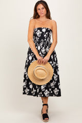 woman wearing a black and white floral strapless midi dress and holding a straw hat