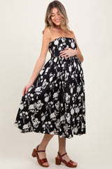 woman wearing a strapless black floral maternity dress, holding her baby bump, styled with brown heeled sandals