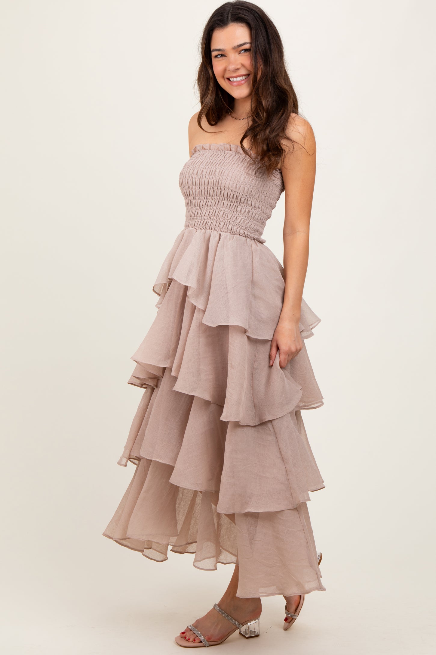 woman wearing a strapless taupe tiered maxi dress with a smocked bodice and ruffled layers