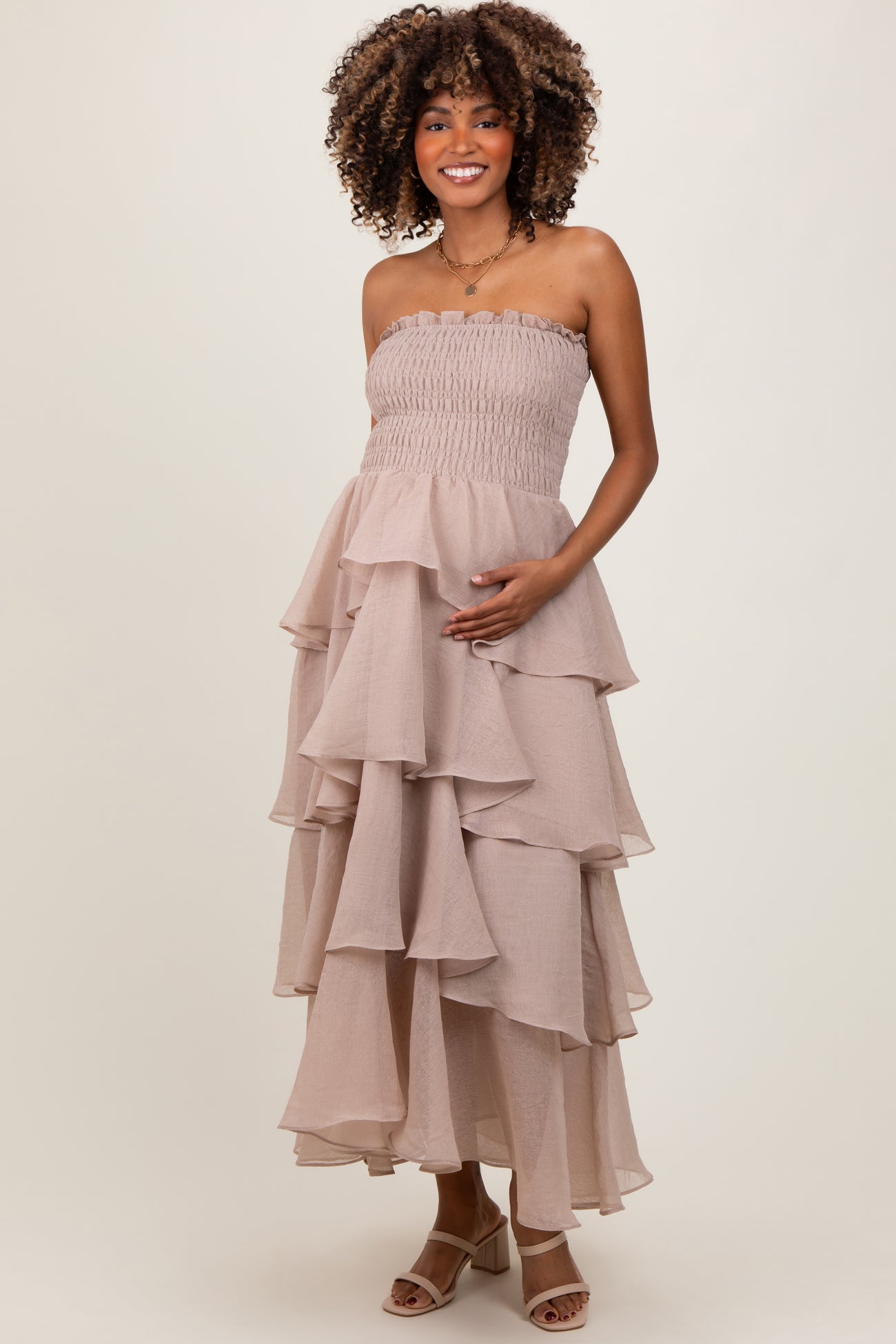 woman wearing a strapless blush maternity maxi dress with layered ruffles and holding her baby bump