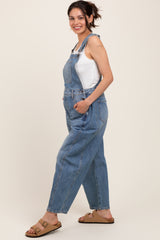 woman wearing maternity denim overalls with a white tank top and brown sandals, no visible baby bump