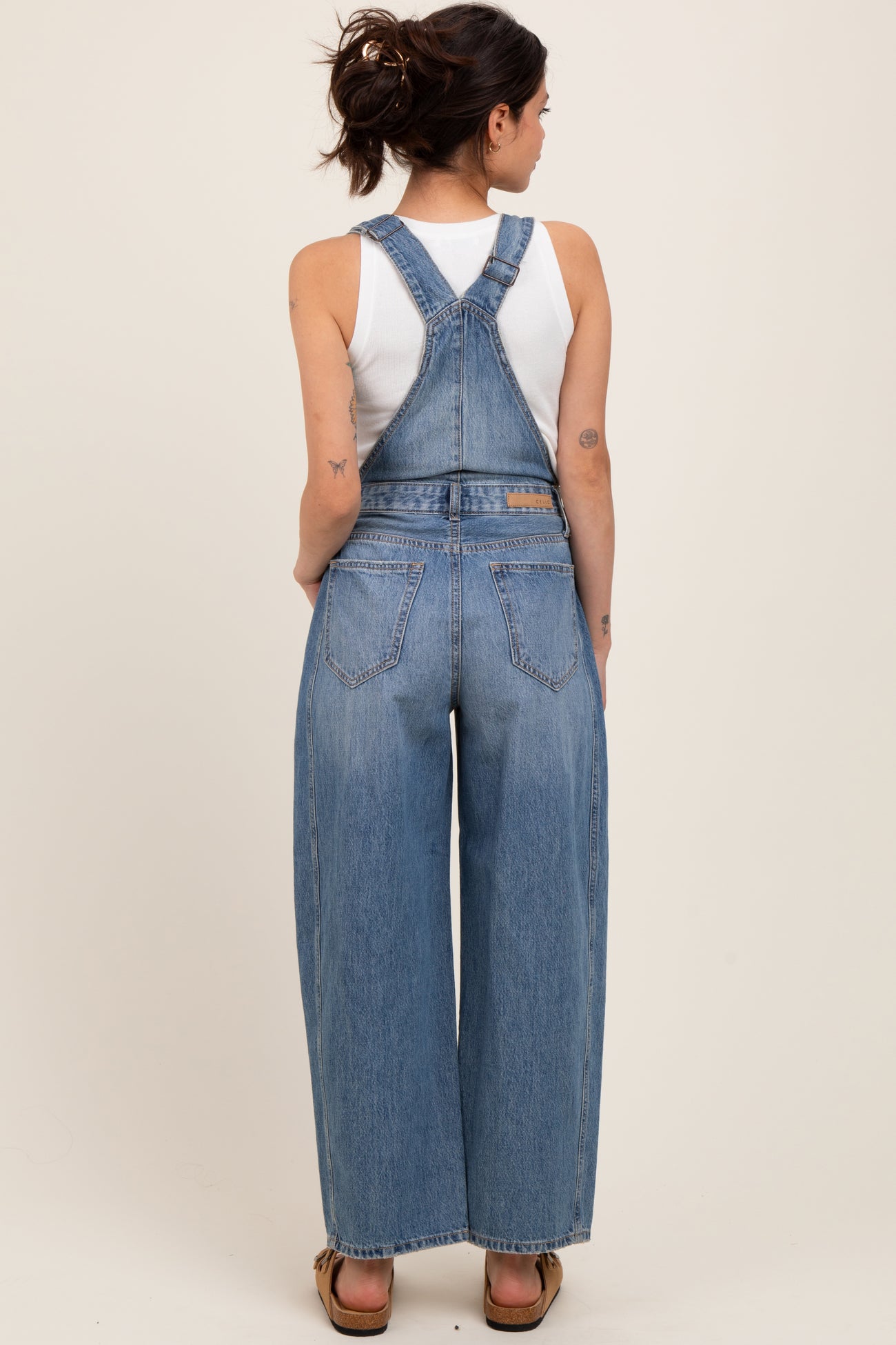 woman wearing a light blue maternity overalls with wide legs and a white tank top underneath, showing a baby bump
