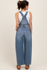 woman wearing a light blue maternity overalls with wide legs and a white tank top underneath, showing a baby bump