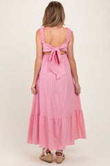 woman wearing a pink and white striped maternity maxi dress with a ruffled back and tie detail