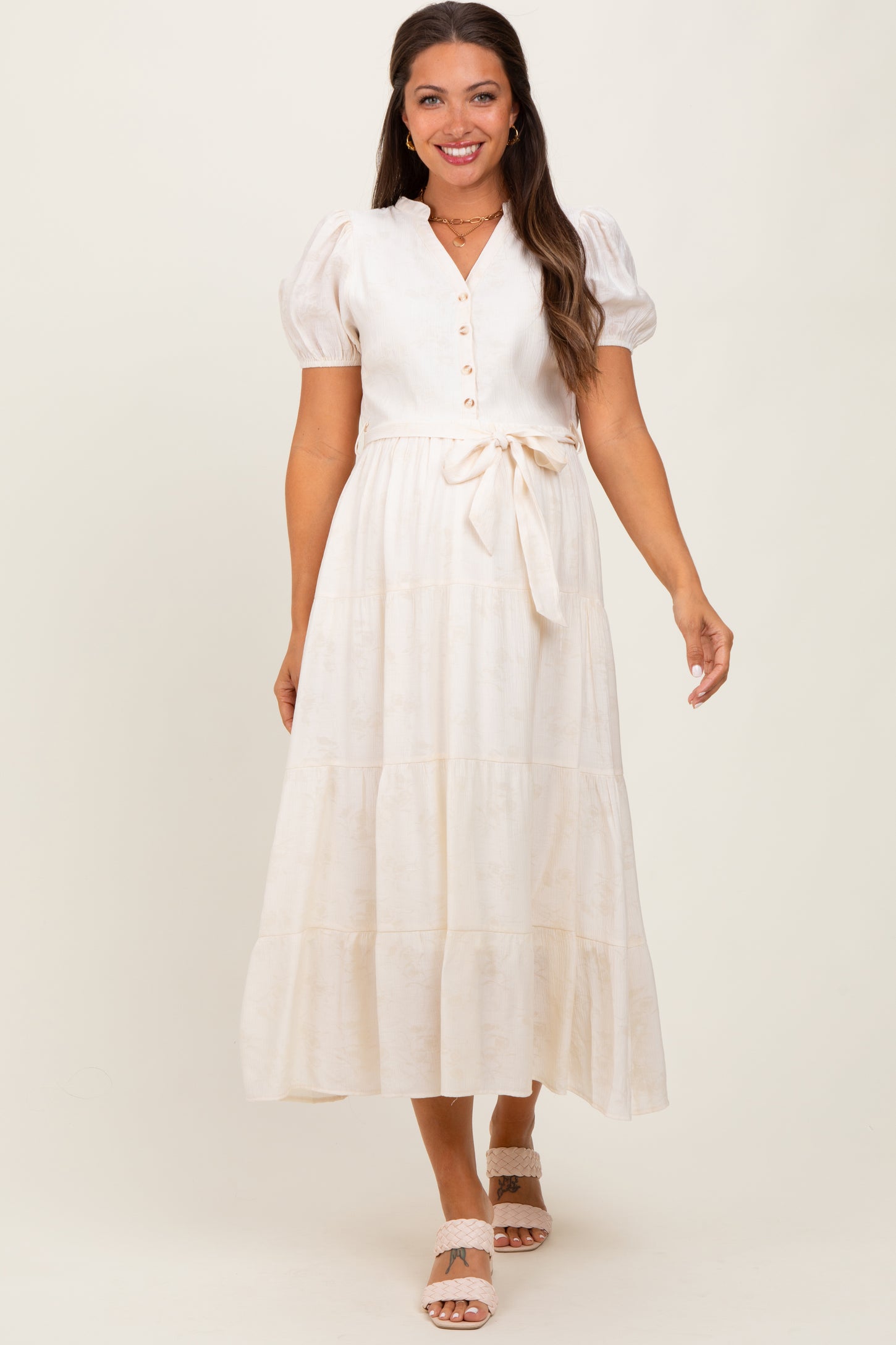 woman wearing a cream maternity dress with puff sleeves, button front, and tie waist detail