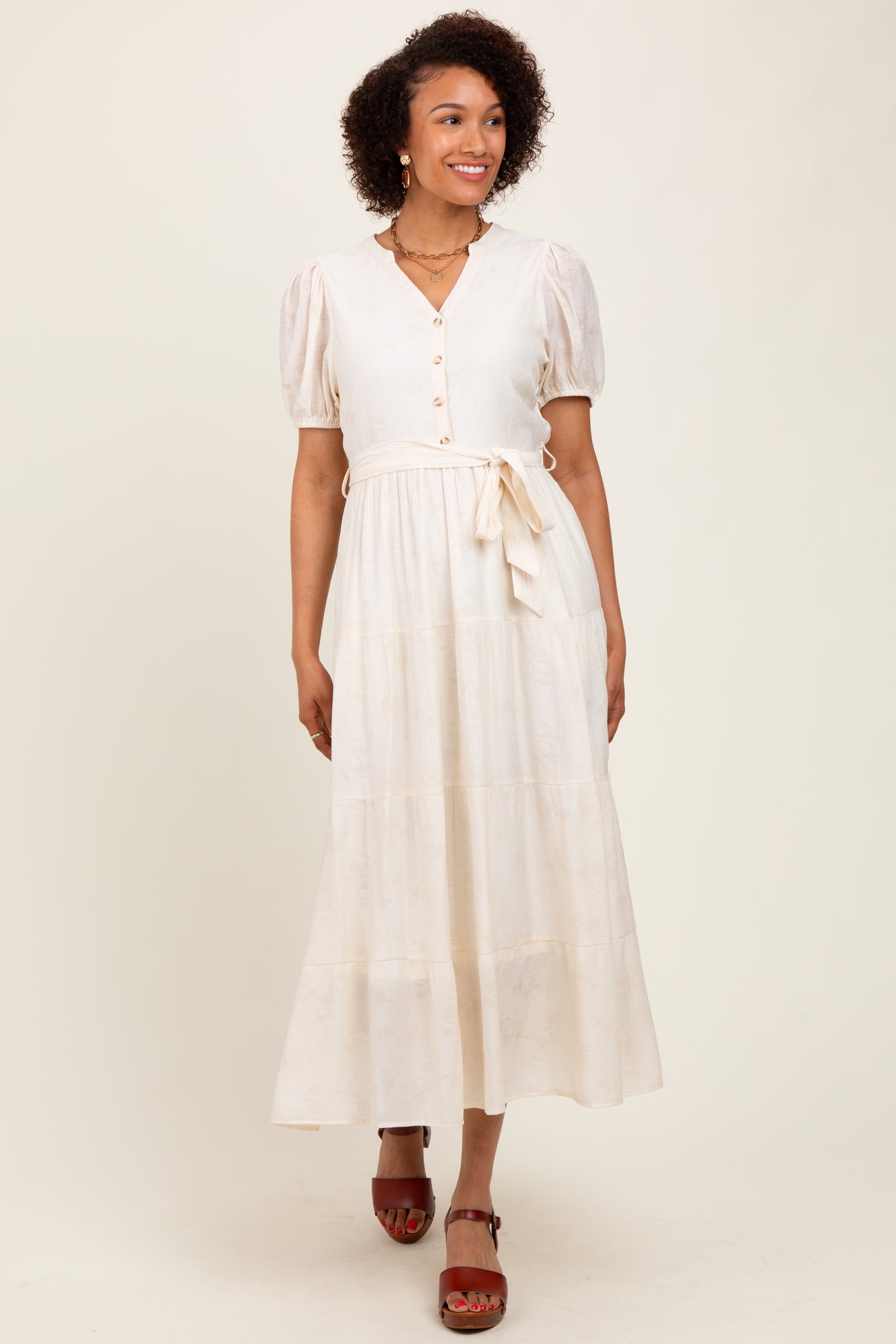 woman wearing a cream long sleeve button-up maxi dress with puff sleeves and a tie waist detail