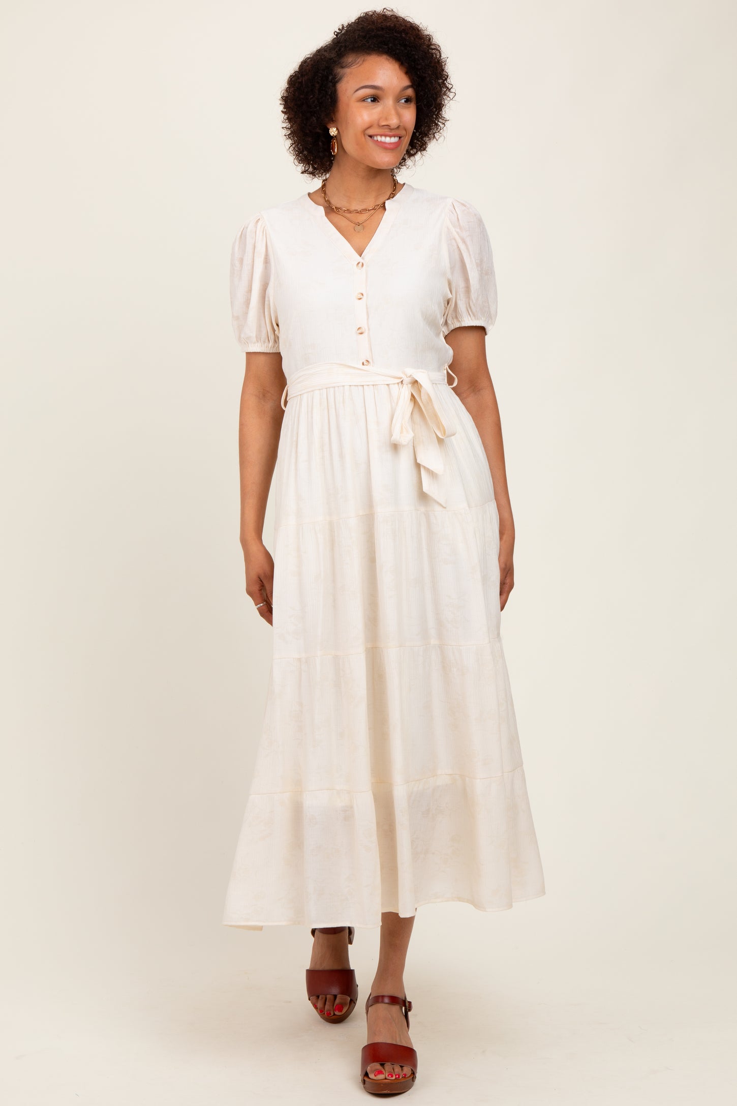 woman wearing a cream long sleeve button-up maxi dress with puff sleeves and a tie waist detail