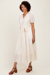 woman wearing a cream-colored button-up midi dress with short puff sleeves and a tie waist detail