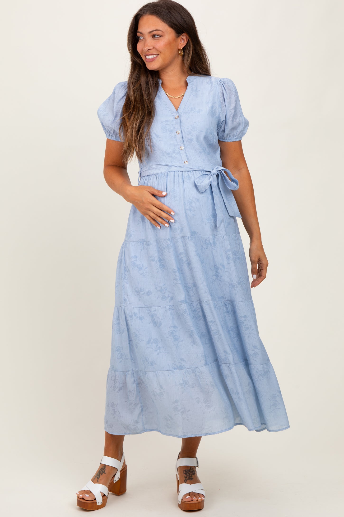 woman wearing a light blue maternity maxi dress with puff sleeves and a tie waist, holding her baby bump