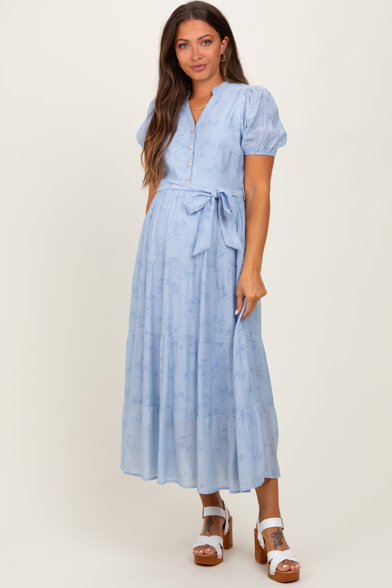 woman wearing a light blue maternity dress with puff sleeves, buttons, and a tied waist detail
