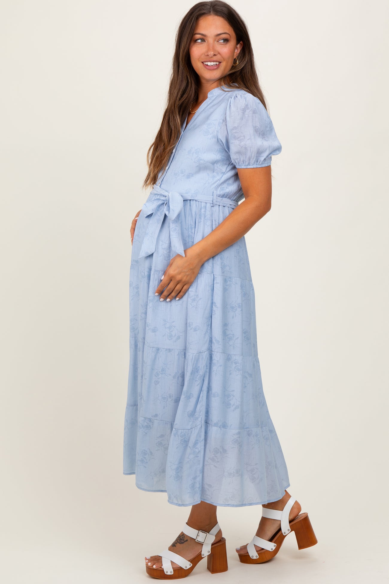woman wearing a light blue floral maternity dress with a tied waist and puff sleeves, standing sideways