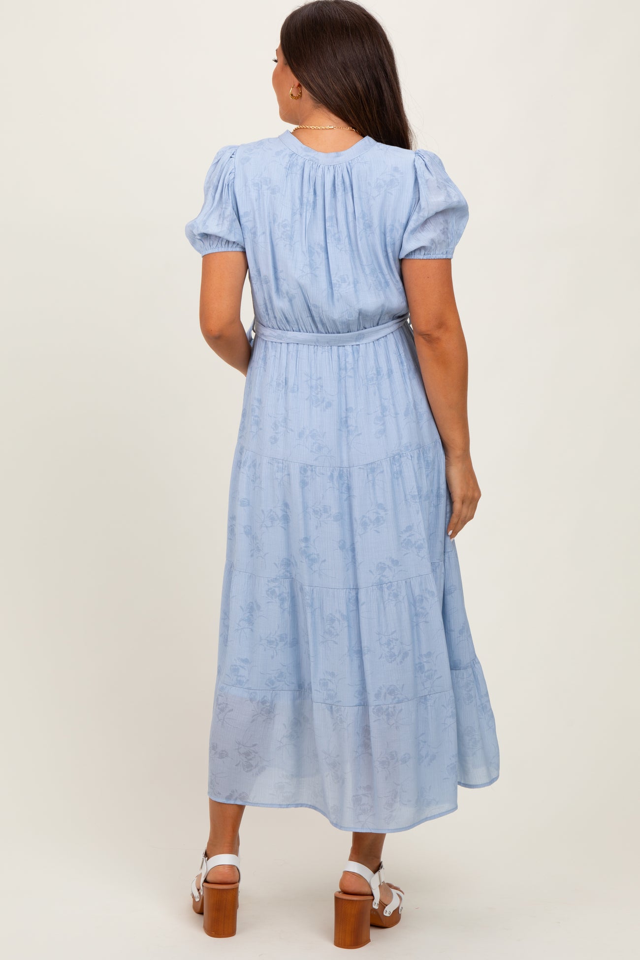 woman wearing a light blue maternity maxi dress with puff sleeves and a cinched waist, showing the back view