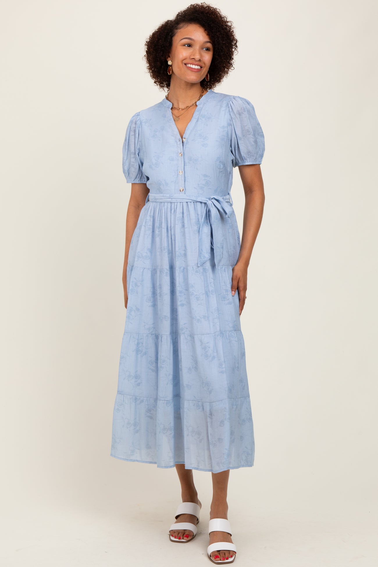 woman wearing a light blue midi dress with puff sleeves and a tie waist standing against a neutral background
