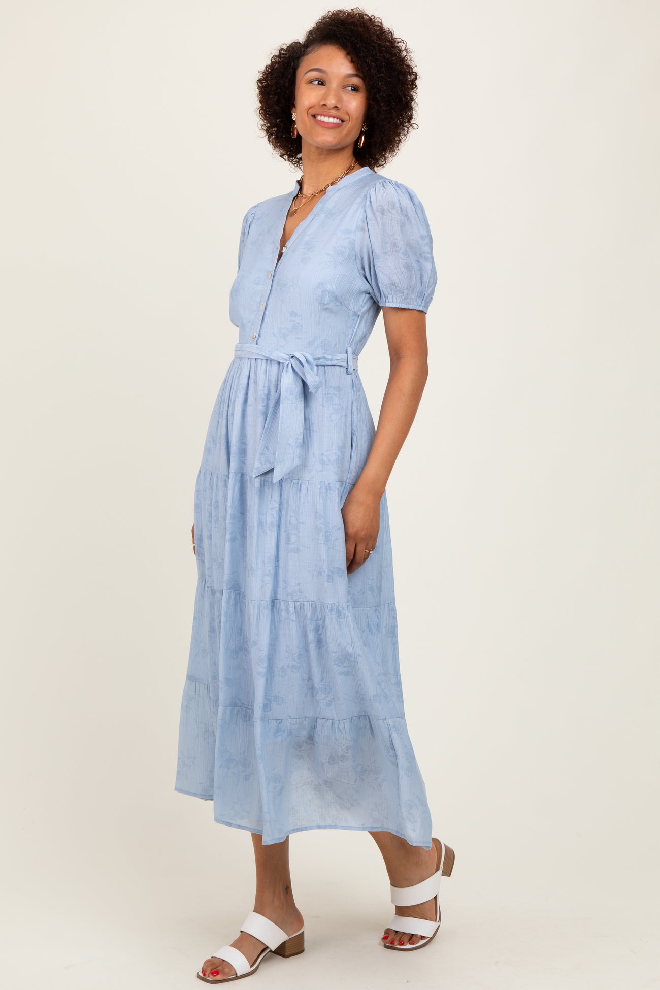 woman wearing a light blue puff sleeve maxi dress with a belt and button details, standing and smiling