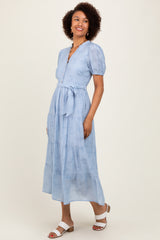 woman wearing a light blue puff sleeve maxi dress with a belt and button details, standing and smiling