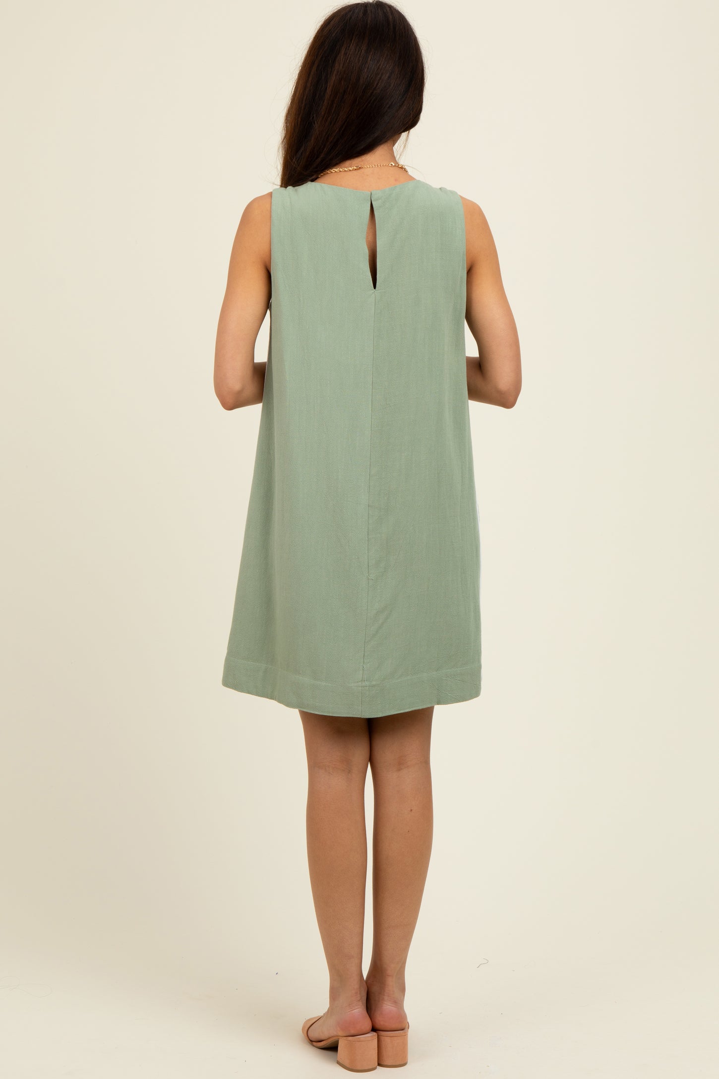 woman wearing a mint green sleeveless shift dress with a keyhole back detail