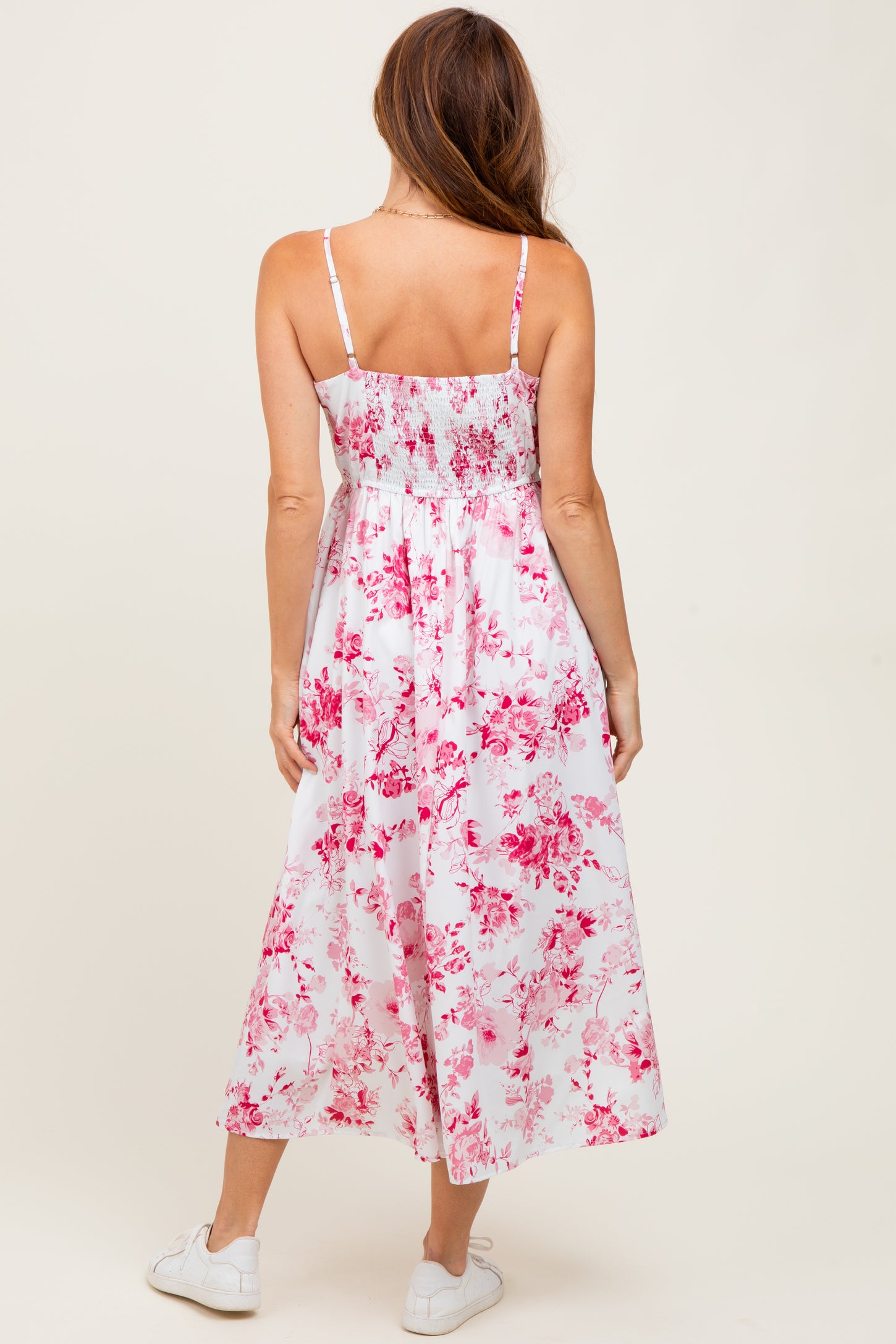 woman wearing a white floral maxi dress with pink patterns and spaghetti straps, seen from the back