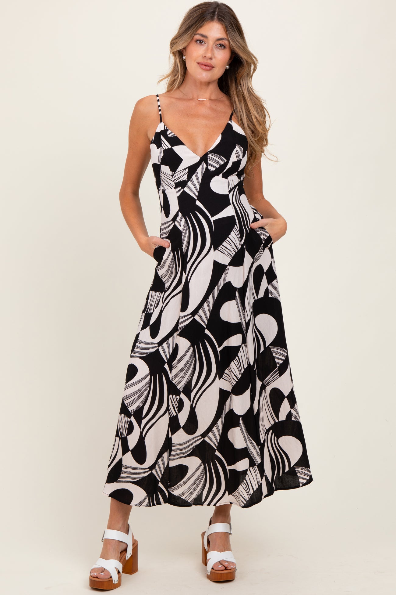 woman wearing a black and white abstract patterned maternity dress with pockets and spaghetti straps