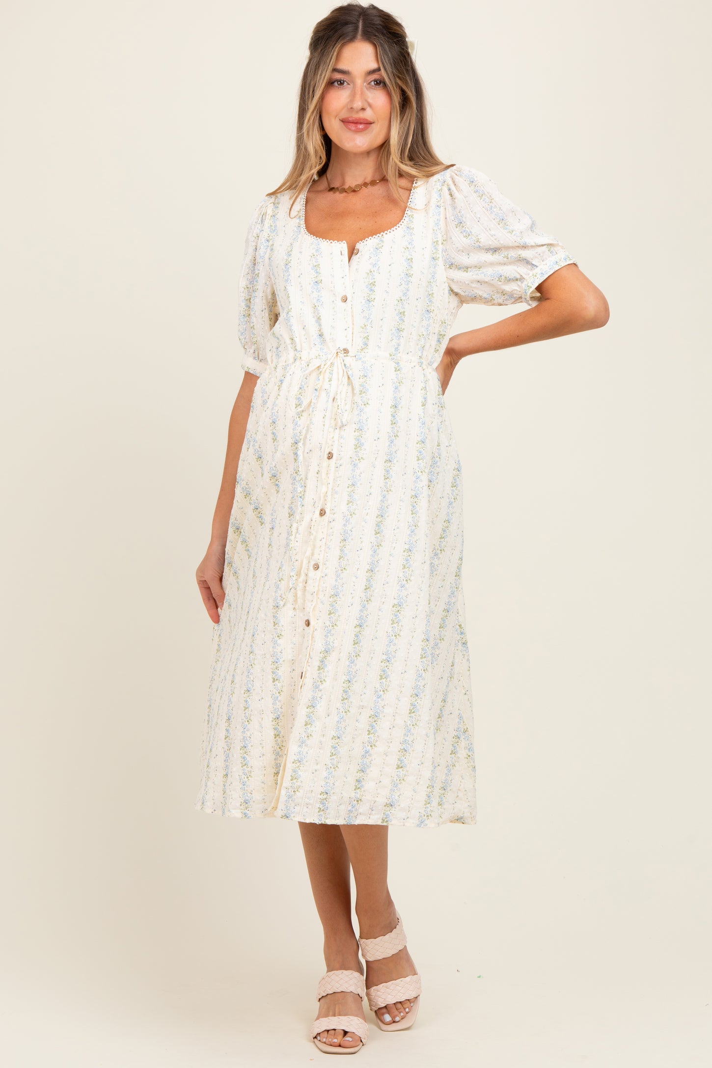 woman wearing a cream floral maternity midi dress with puff sleeves and button front, showcasing her baby bump
