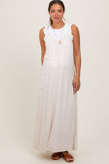 woman wearing a light beige maternity maxi dress with ruffled straps and side pockets, standing in a relaxed pose