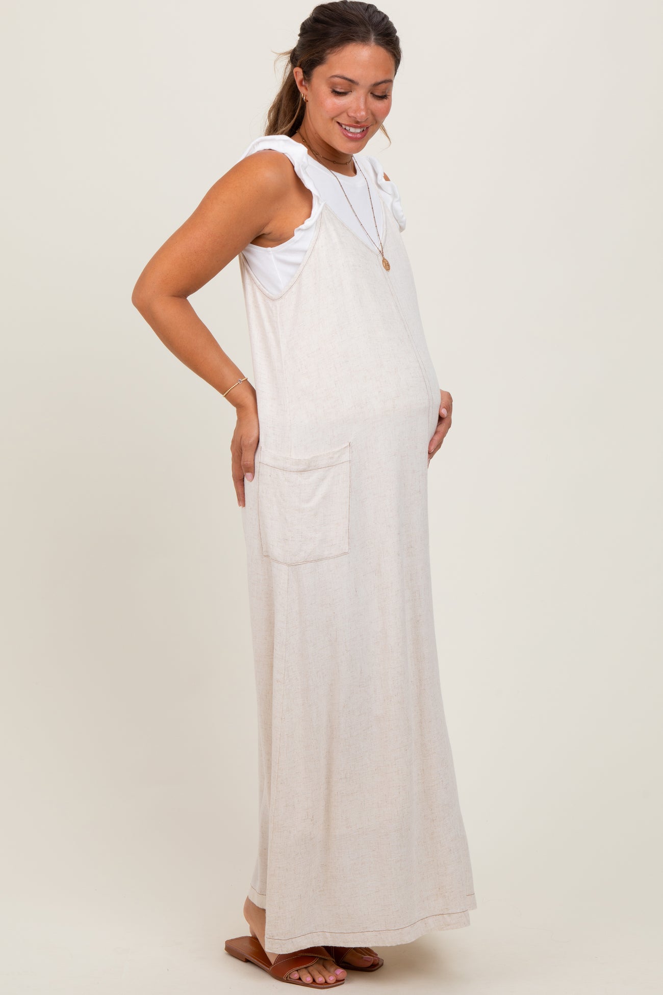 woman wearing a light beige maternity maxi dress with ruffle straps, smiling and showing her baby bump
